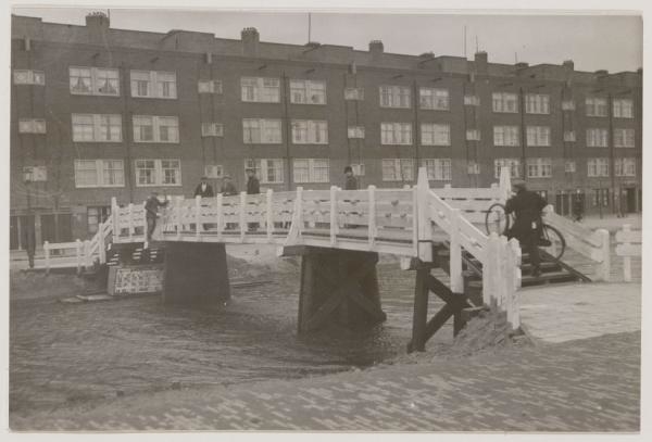 Houten Voetbrug. Houten voetbrug 115 over de Ringvaart, gezien vanaf de Ooster Ringdijk naar Valentijnkade 4-18 (v.l.n.r.). Deze houten brug lijkt erg op het bruggetje zoals die gelegen moeten hebben bij de Schalk Burgerstraat.<br />Bron: Beeldbank Stadsarchief Amsterdam. 