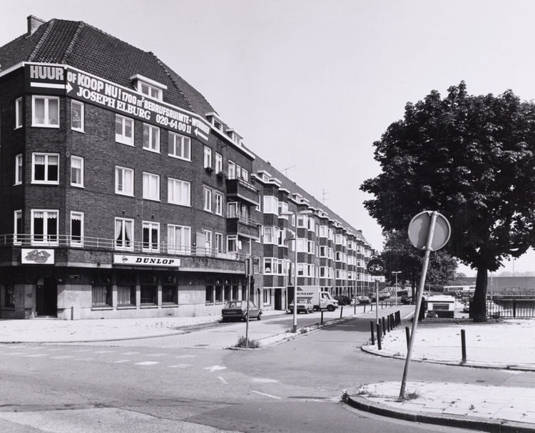  Schollenbrugstraat/hoek Weesperzijde 1985. Nadat de garage was gesloopt kwamen deze woningen met op de begane grond bedrijven ervoor in de plaats. Dunlop (rubber banden en matrassen)  was de hoofdhuurder van de bedrijfspanden.<br />Foto: Beeldbank Stadsarchief Amsterdam 
