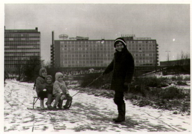 Slee Op de slee bij de Ringdijk, op het terrein van de vrogere volkstuintjes. Kees trekt de slee, op de slee zitten zijn zus Thea en buurmeisjes Karin en Sandrs. Op de achtergrond Hotel Casa 400. Ongeveer 1964. 
