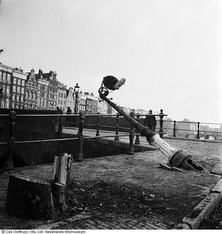 Hongerwinter. Boomstronk en een omgevallen straatlantaarn nabij een stadsbrug in de hongerwinter, Amsterdam (1944-1945). Maker van de foto is Cas Oorthuys, bron: www.geheugenvannederland.nl 