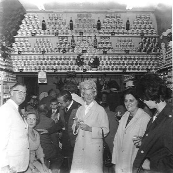  De opening van de winkel van Jannies ouders in 1965 - links staat de heer Wijnbergh, daarnaast zit Jannies moeder. Naast haar staan meneer en mevrouw de Beer, van Bakker de Beer. Daarnaast weer een buurvrouw met haar dochter. 