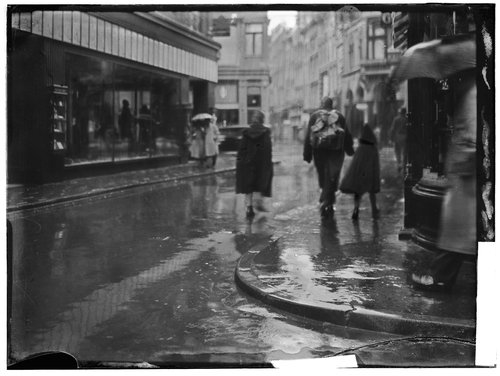 Maison de Vries. Links op de foto de winkel waar Levie werkte: Maison de Vries, Kalverstraat 125-127. Op de voorgrond de ingang van de Rozenboomsteeg. Voorbijgangers, gezien op de rug, met paraplu's en regenjassen lopen in de regen.<br />Foto gemaakt door: Bernard F. Eilers <br />Datering 1935 ca., bron: Beeldbank, Stadsarchief Amsterdam. 