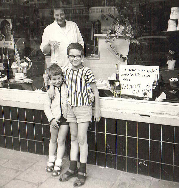 Roberto en Giovanni Massaro voor de ijswinkel Giovanni als kind voor de ijssalon van zijn ouders. In de winkel glimlacht mevrouw Massaro.<br />foto Giovanni Massaro. Achter de etalage staat hun moeder, Aaf Masssaro. Foto: 1964. 