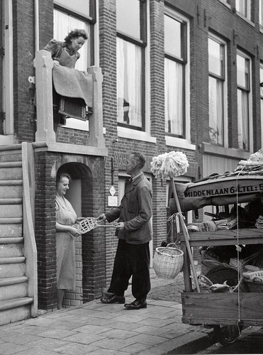  Handelaar in huishoudelijk artikelen gaat langs de deuren met zijn koopwaren, Amsterdam, Nederland 23 oktober 1953. Foto: De handelaar toont een mattenklopper aan nieuwsgierige huisvrouwen.  Foto afkomstig uit nationaal archief Spaarnestad 