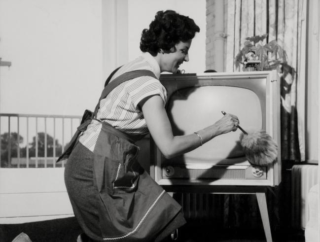 Televisie.. Een huisvrouw met schort aan is met een plumeau bezig een TV / televisietoestel af te stoffen. Foto afkomstig uit Nationaal archief Spaarnestad 