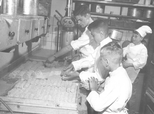  Van jong tot oud: iedereen moest meehelpen. Dolf, Jos, John en René hier in de bakkerij bezig met het doorhalen van kroketten. 