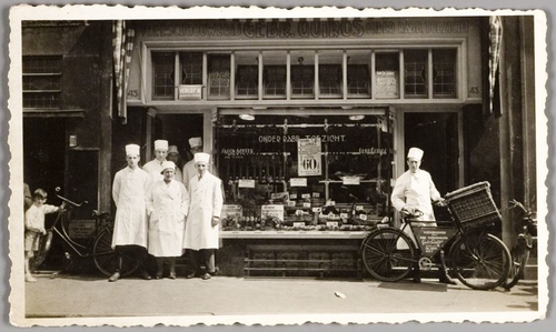 Slagerij Quiros Jodenbreestraat. Foto van de gevel van vleeswarenhandel Quiros aan de Jodenbreestraat, nr. 43, met de slagers en slagersjongen met fiets, circa 1938. Bron: JHM 