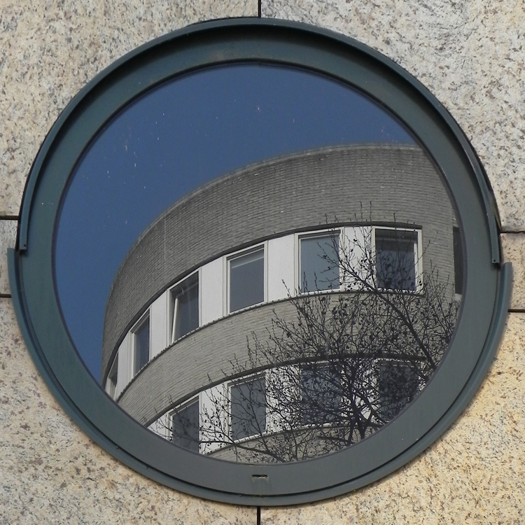 Een cirkelvormig raam,met spiegelend daarin een rond gebouw.  