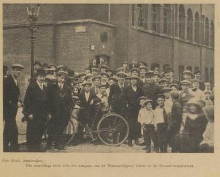 Foto van Kisch in De Joodsche Prins van 15 aug. 1912. Groep mensen voor de diamantfabriek van Coster in de Zwanenburgerstraat.  